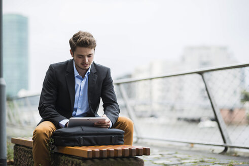 Deutschland, Hessen, Frankfurt, junger Mann sitzt auf einer Bank und benutzt sein digitales Tablet - UUF001888