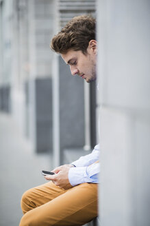 Deutschland, Hessen, Frankfurt, Porträt eines sitzenden jungen Mannes, der sein Smartphone benutzt - UUF001837