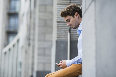 Deutschland, Hessen, Frankfurt, Porträt eines sitzenden jungen Mannes, der sein Smartphone benutzt - UUF001838