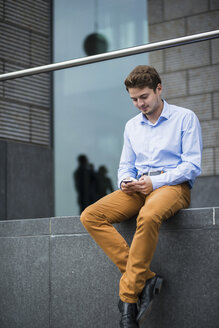 Deutschland, Hessen, Frankfurt, Porträt eines sitzenden jungen Mannes, der sein Smartphone benutzt - UUF001839
