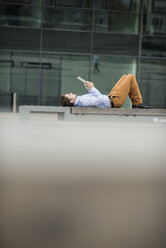 Germany, Hesse, Frankfurt, young man lying on back using his digital tablet - UUF001847