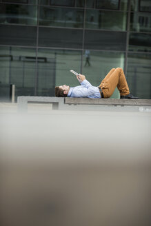 Deutschland, Hessen, Frankfurt, junger Mann liegt auf dem Rücken und benutzt sein digitales Tablet - UUF001847