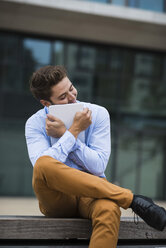 Germany, Hesse, Frankfurt, portrait of young man hugging his digital tablet - UUF001842