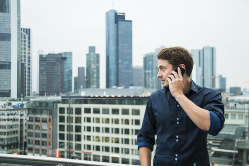 Deutschland, Hessen, Frankfurt, junger Mann beim Telefonieren mit seinem Smartphone vor der Skyline - UUF001844