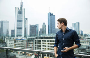 Germany, Hesse, Frankfurt, young man with his smartphone standing in front of the skyline - UUF001845