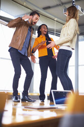 Drei glückliche kreative Menschen tanzen auf einem Konferenztisch - ZEF000912