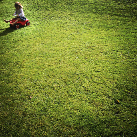 Mädchen mit Bobbycar auf Wiese, lizenzfreies Stockfoto