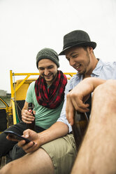 Two friends drinking beer and looking at cell phone outdoors - UUF001855