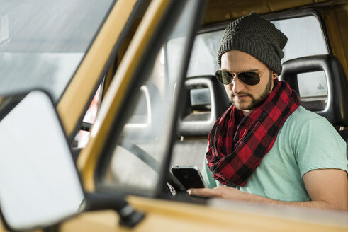 Junger Mann mit Mobiltelefon im Pick-up sitzend - UUF001891