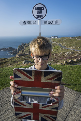 Vereinigtes Königreich, Cornwall, Junge, der mit seinem digitalen Tablet ein Selfie vor dem Wegweiser in Land's End macht, lizenzfreies Stockfoto
