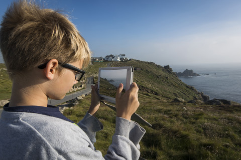 UK, Cornwall, Junge fotografiert Landschaft am Land's End mit seinem digitalen Tablet, lizenzfreies Stockfoto