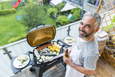 Lächelnder Mann beim Grillen auf seinem Balkon - MBEF001274