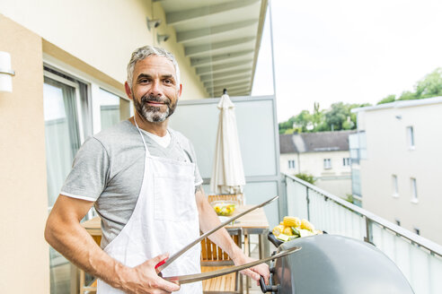 Portrait of smiling man with apron and tongs on his balcony - MBEF001280