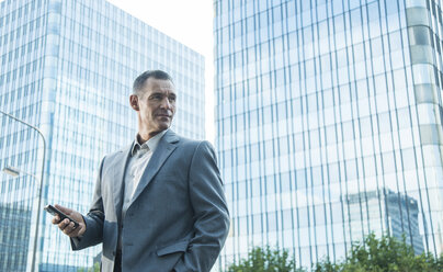 Mature businessmanwith cell phone outside office building - UUF001943