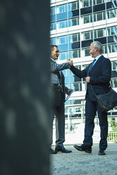Zwei Geschäftsleute schütteln sich vor einem Bürogebäude die Hände - UUF001945