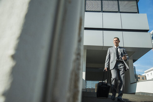 Geschäftsmann mit Koffer vor Bürogebäude - UUF001950