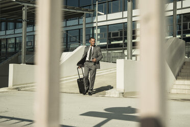 Businessman with suitcase outside office building - UUF001952