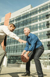 Two businessmen playing basketball outside office building - UUF001955