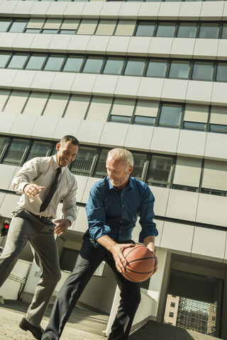 Two businessmen playing basketball outside office building stock photo