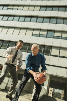 Zwei Geschäftsleute spielen Basketball vor einem Bürogebäude - UUF001959