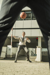 Zwei Geschäftsleute spielen Basketball vor einem Bürogebäude - UUF001961