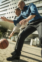 Zwei Geschäftsleute spielen Basketball vor einem Bürogebäude - UUF001963