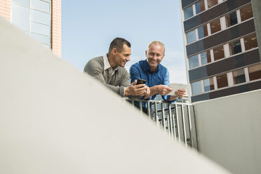 Zwei Geschäftsleute vor einem Bürogebäude, die ein Mobiltelefon und ein digitales Tablet benutzen - UUF001960