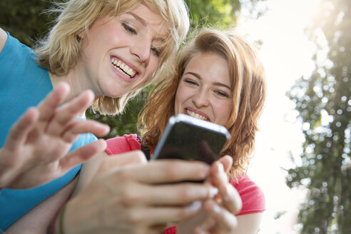 Deutschland, Berlin, Junge Frauen benutzen Smartphone im Park - FKF000654