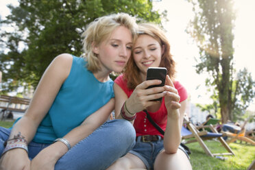 Deutschland, Berlin, Junge Frauen benutzen Smartphone im Park - FKF000655