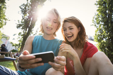 Deutschland, Berlin, Junge Frauen benutzen Smartphone im Park - FKF000656