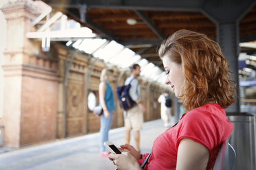 Deutschland, Berlin, Junge Frau benutzt Smartphone am Bahnhof - FKF000657