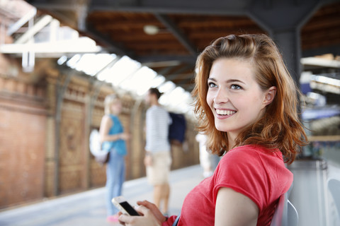 Deutschland, Berlin, Junge Frau benutzt Smartphone am Bahnhof, lizenzfreies Stockfoto