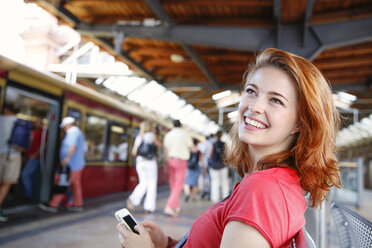 Germany, Berlin, Young woman using smart phone at train station - FKF000659