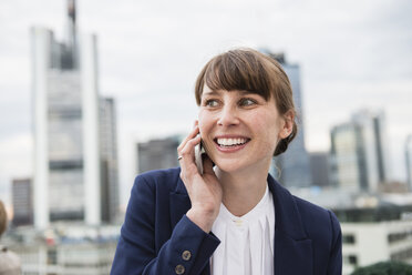 Deutschland, Hessen, Frankfurt, Porträt einer lächelnden Geschäftsfrau beim Telefonieren vor einer Skyline - FMKYF000519