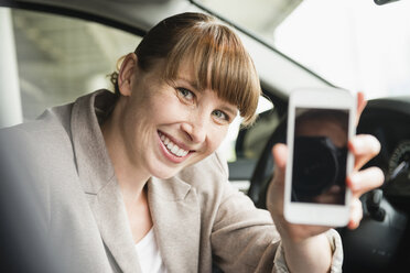 Porträt einer lächelnden Geschäftsfrau, die in einem Auto sitzt und ihr Smartphone zeigt - FMKYF000532