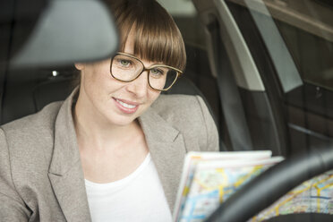 Portrait of smiling businesswoman sitting in a car looking at city map - FMKYF000534