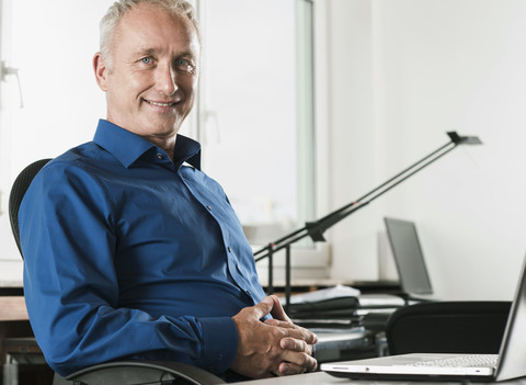 Porträt eines lächelnden Geschäftsmannes am Schreibtisch, lizenzfreies Stockfoto