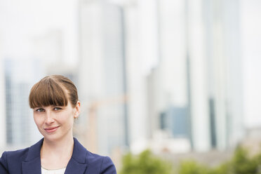 Portrait of smiling businesswoman in front of skyscrapers - FMKYF000543