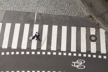 Germany, businesswoman with rolling suitcase walking on zebra crossing, view from above - FMKYF000550