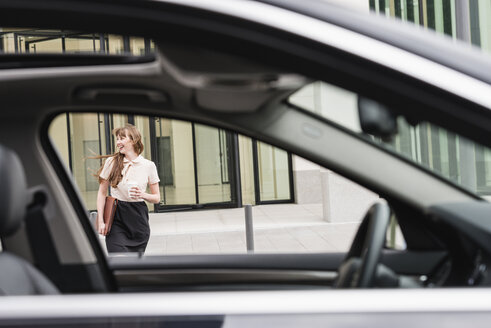 Germany, Hesse, Frankfurt, happy businesswoman walking with coffee to go behind a car - FMKYF000562