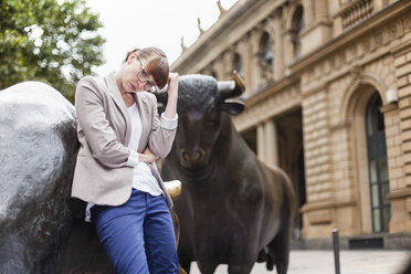 Germany, Hesse, Frankfurt, portrait of pansive businesswoman standing in front of stock market - FMKYF000572