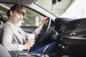 Deutschland, Hessen, Frankfurt, Porträt einer lächelnden Geschäftsfrau am Steuer eines Autos mit einem Coffee to go in einer Hand - FMKYF000575