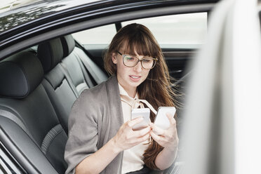 Deutschland, Geschäftsfrau im Auto sitzend mit zwei Smartphones - FMKYF000584