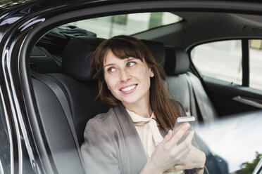 Deutschland, Porträt einer lächelnden Geschäftsfrau, die mit einem Smartphone in einem Auto sitzt - FMKYF000585