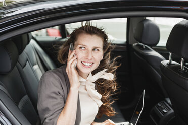 Deutschland, Porträt einer lächelnden Geschäftsfrau, die in einem Auto sitzt und mit einem Smartphone telefoniert - FMKYF000586