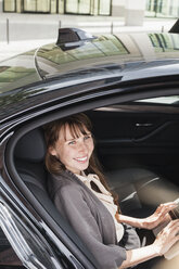 Deutschland, Porträt einer lächelnden Geschäftsfrau, die in einem Auto sitzt und einen Laptop benutzt - FMKYF000588