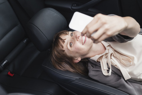 Deutschland, Porträt einer lächelnden Geschäftsfrau, die in ihrem Auto ein Selfie mit ihrem Smartphone macht, lizenzfreies Stockfoto