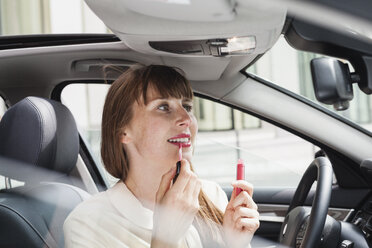 Portrait of businesswoman sitting in her car applying lipstick - FMKYF000593