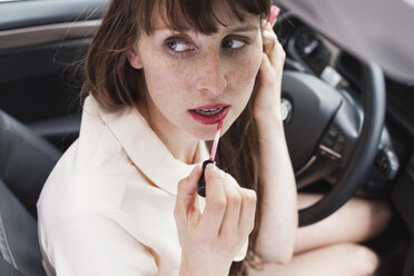 Portrait of businesswoman sitting in her car applying lipstick - FMKYF000594