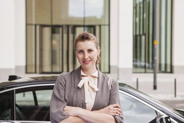 Portrait of smiling businesswoman with crossed arms standing in front of an office building - FMKYF000597